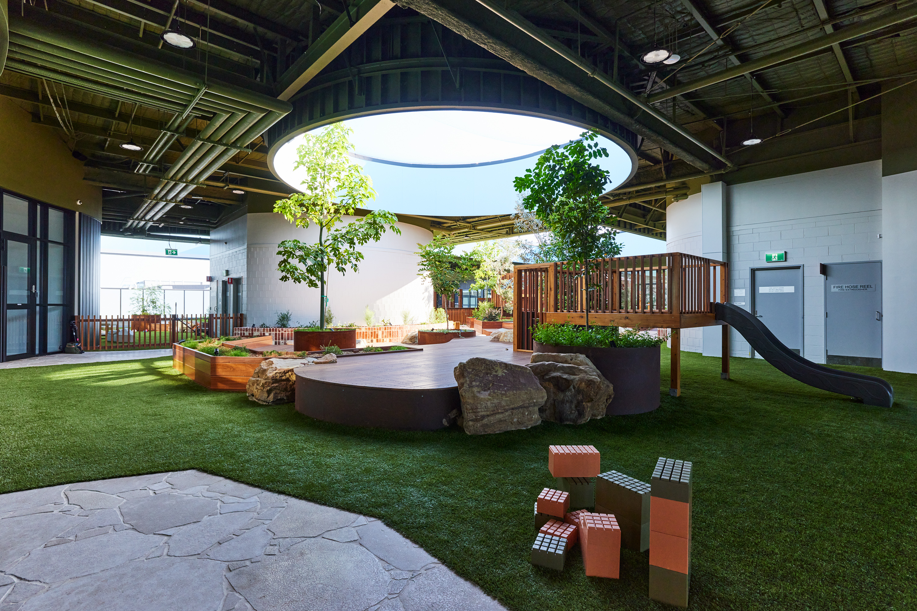 Open-air play space with mature trees growing through circular roof opening