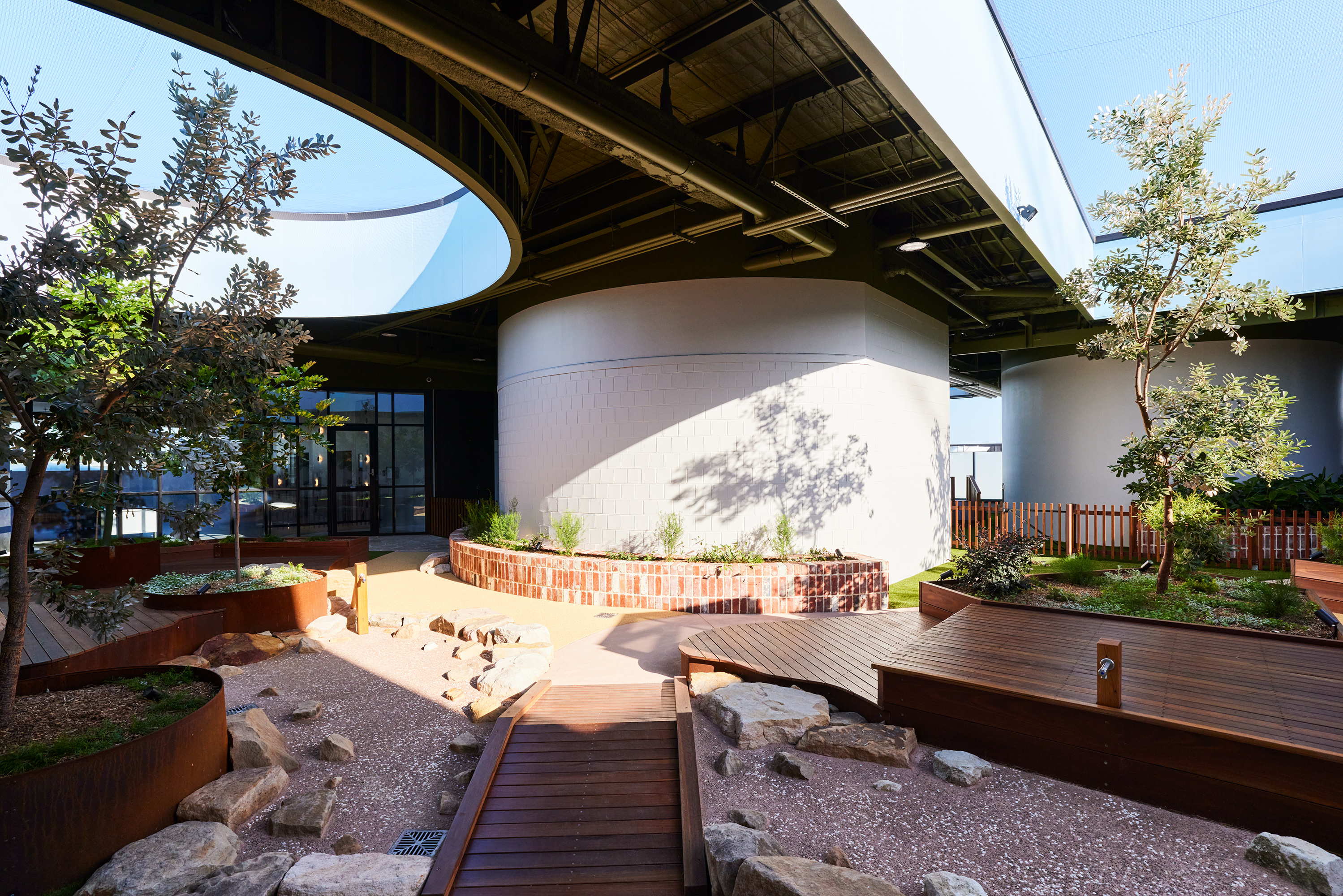 Outdoor courtyard with timber boardwalk, sandstone rocks and corten planters