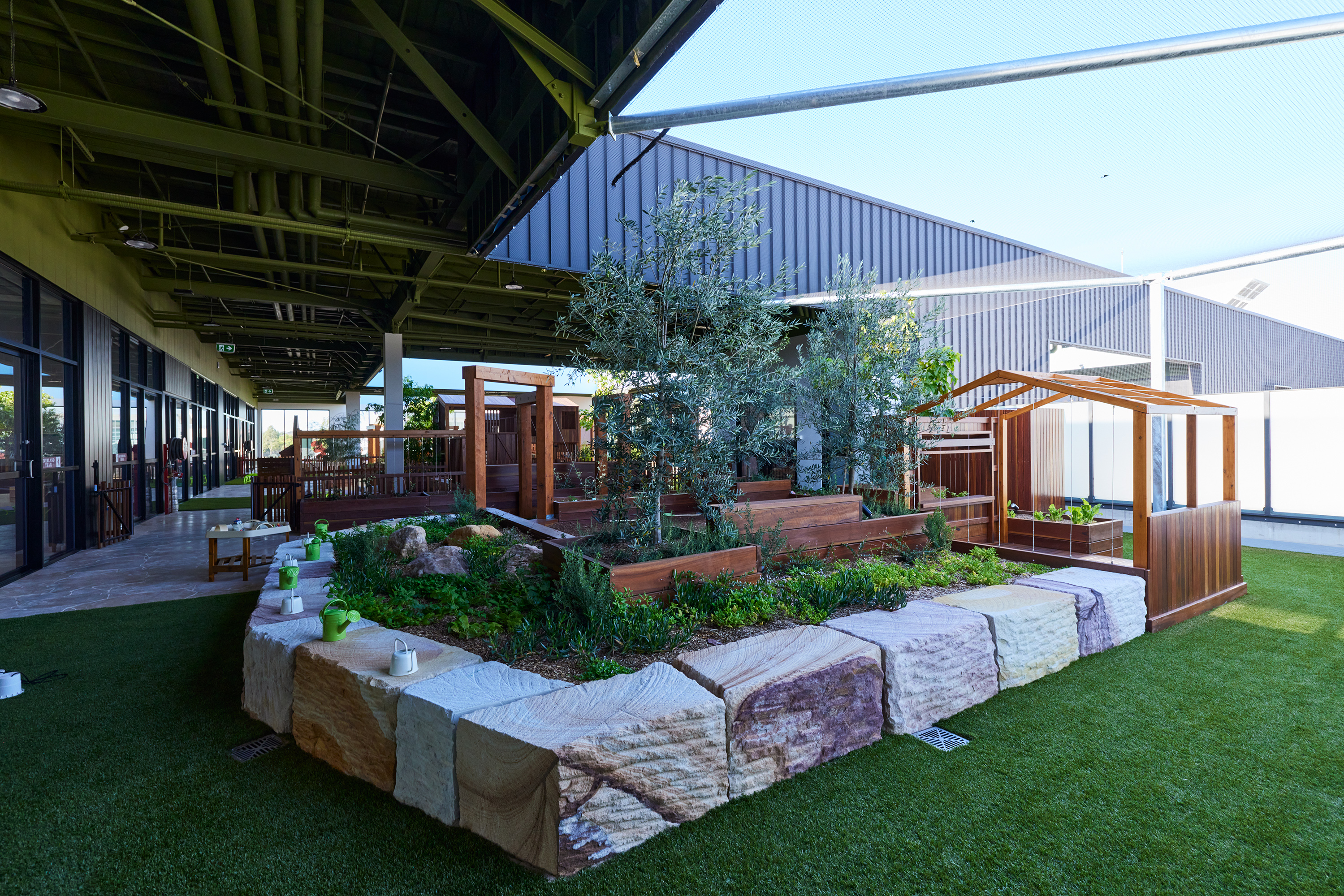 Timber play structure adjacent to sand pit with lush green plantings