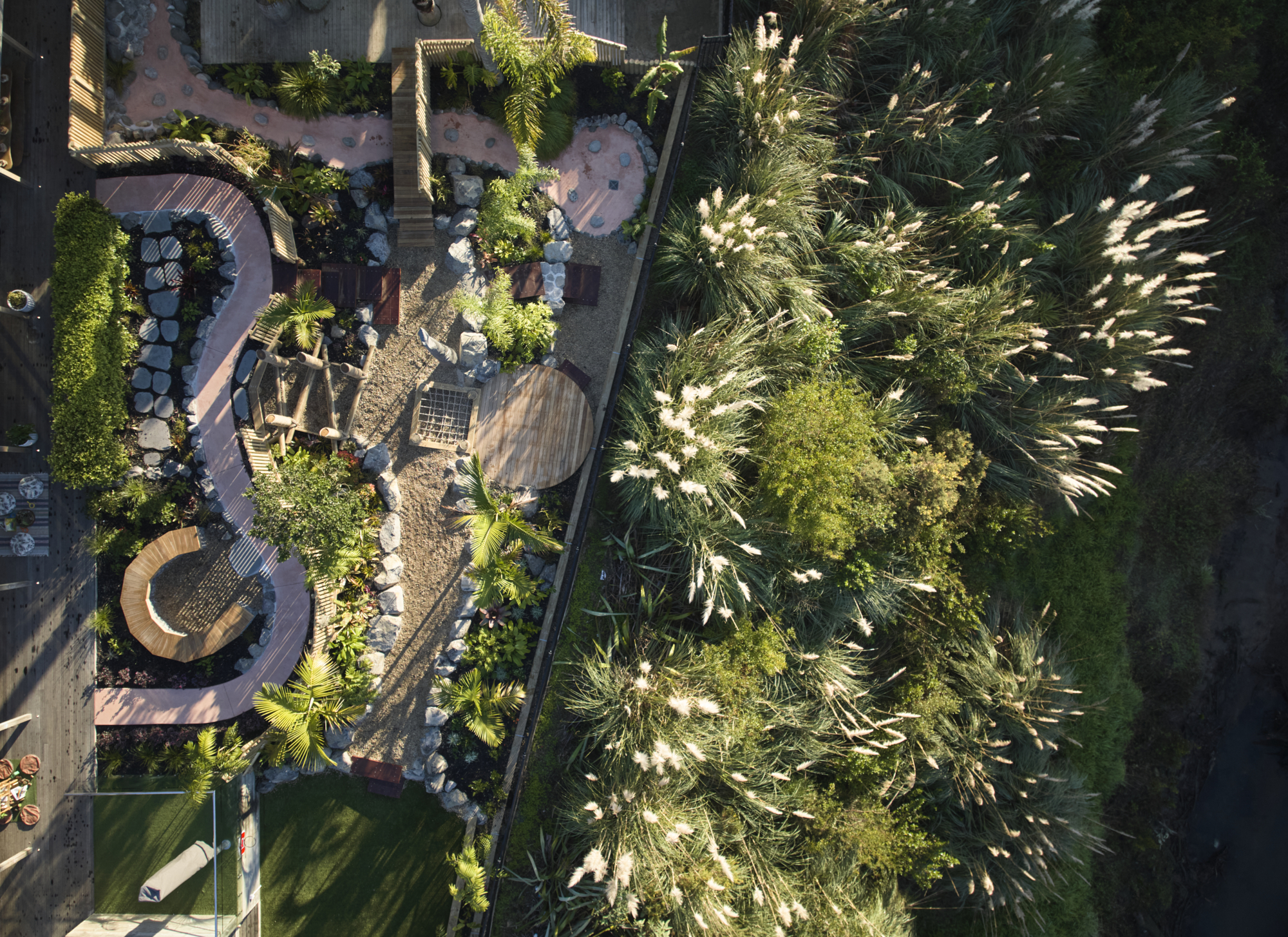 Aerial view of playground showing curved pathways, stone boulders, timber structures and dense tropical plantings