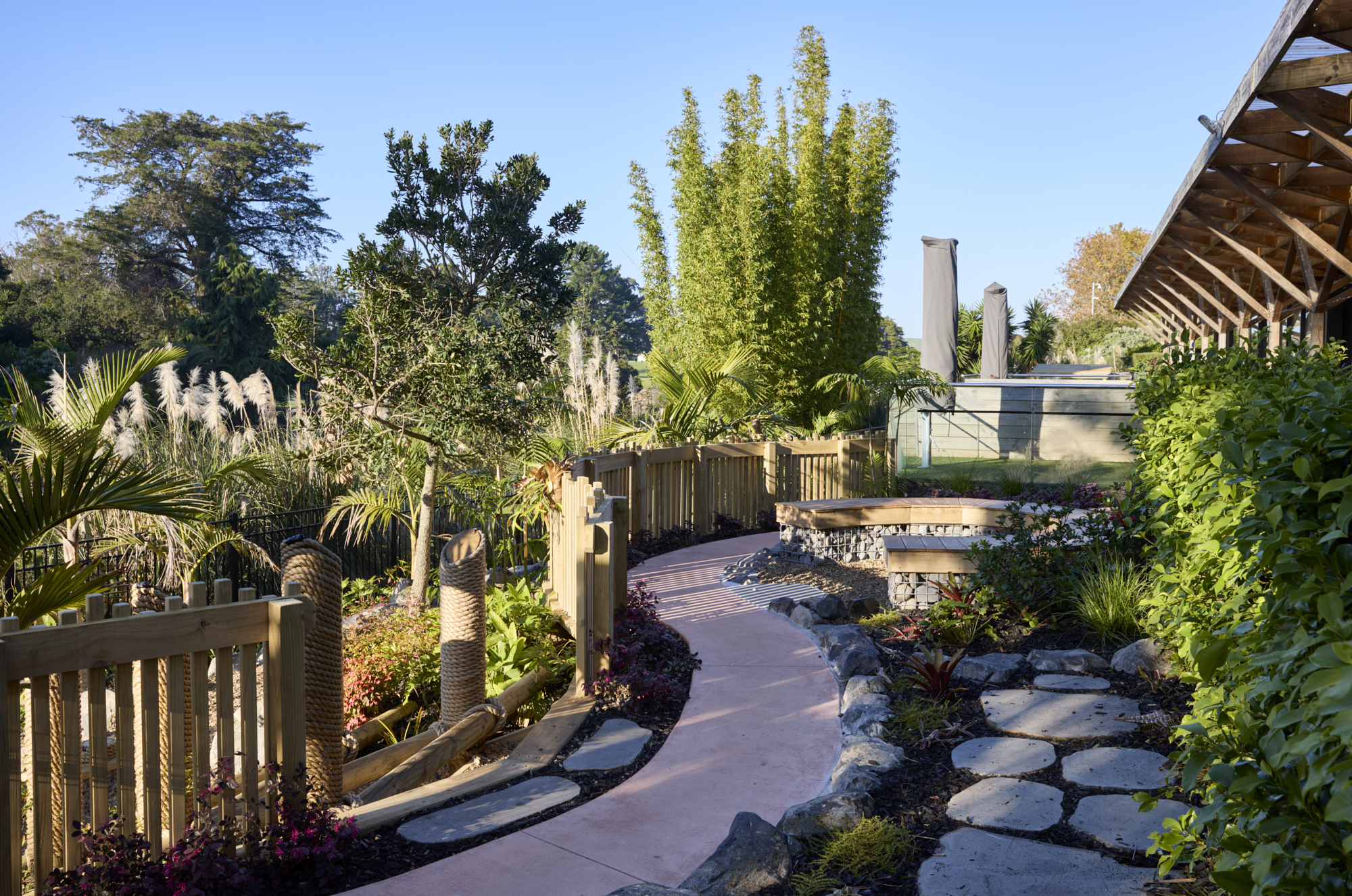 Coloured pathway winding through planted areas with stone stepping pads, timber seating and pergola structure