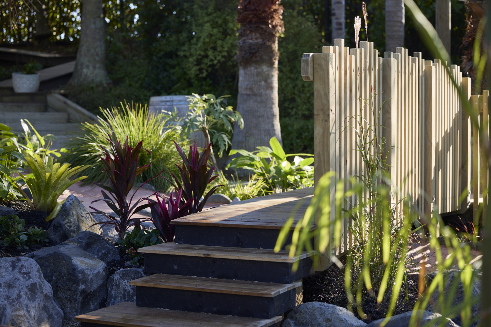 Timber steps with stone boulders, red-leafed plants and timber picket fencing between play zones