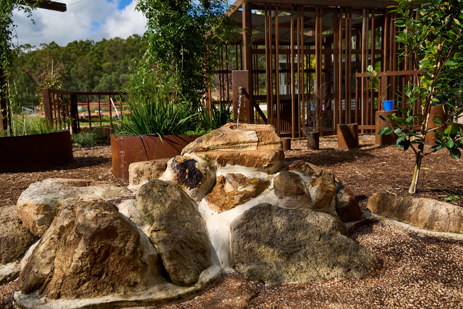 Sandstone boulder water play area with timber cubby behind