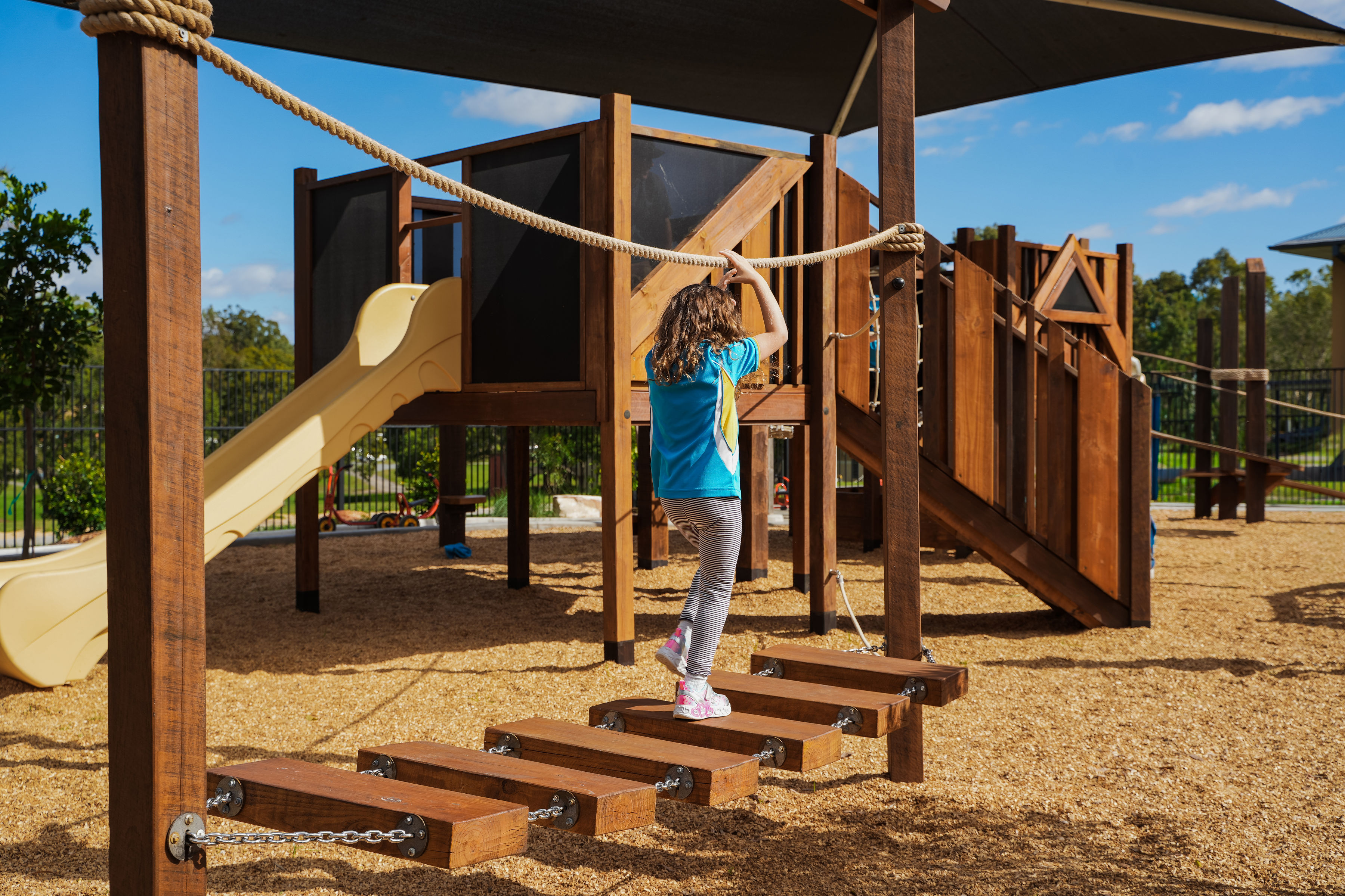 A child crossing the chain-linked stepping bridge to the play tower