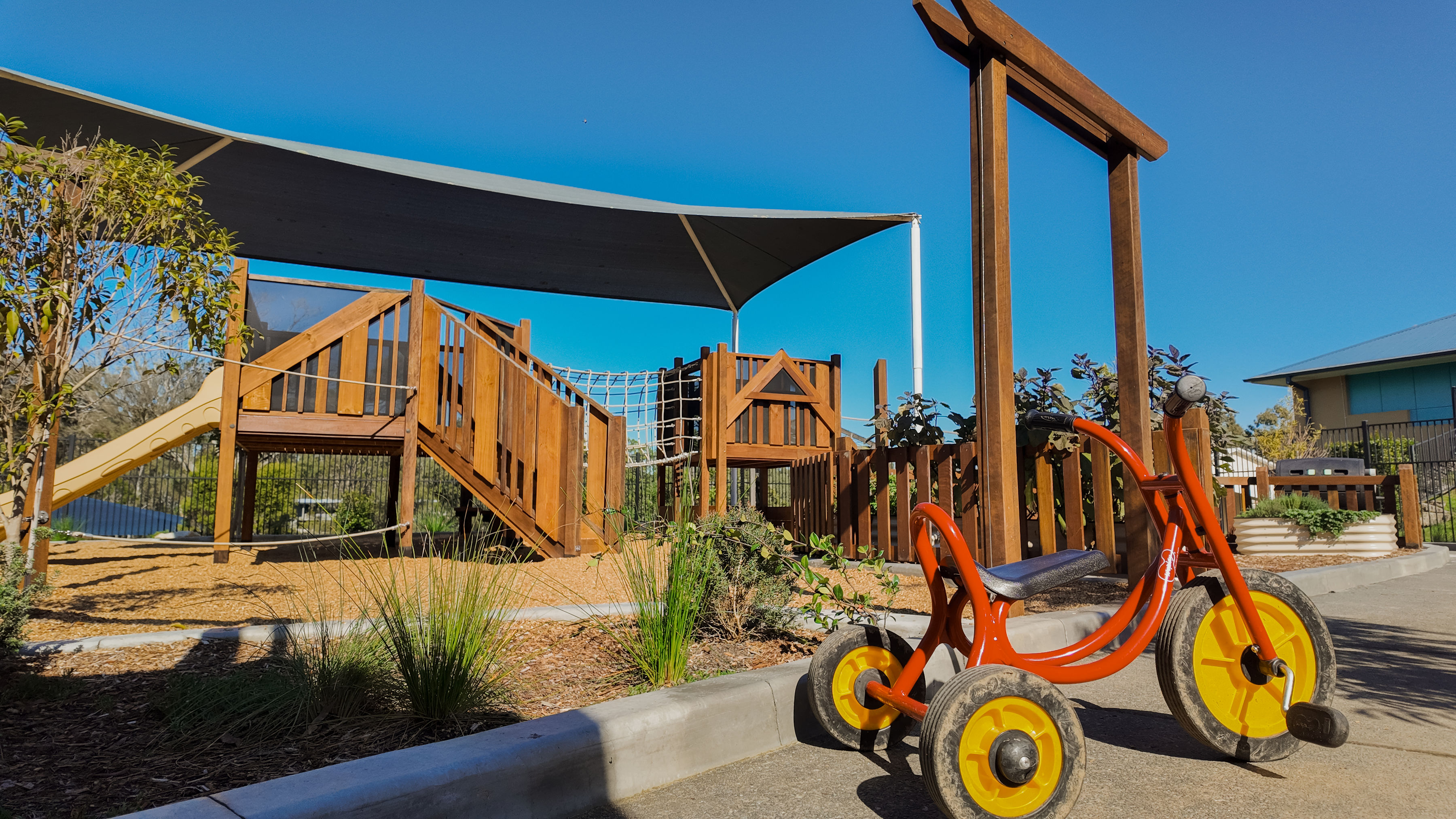 A tricycle parked near the garden pergola and play tower