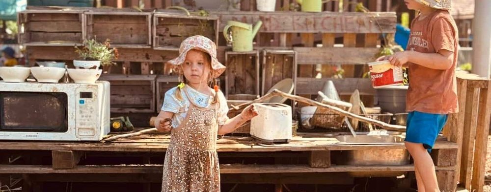 Two children playing together at an outdoor mud kitchen