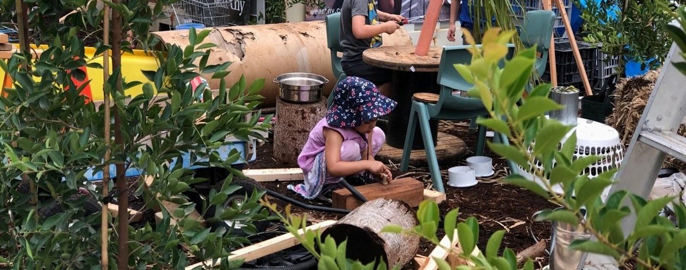 Child playing with loose parts in a leafy outdoor play space