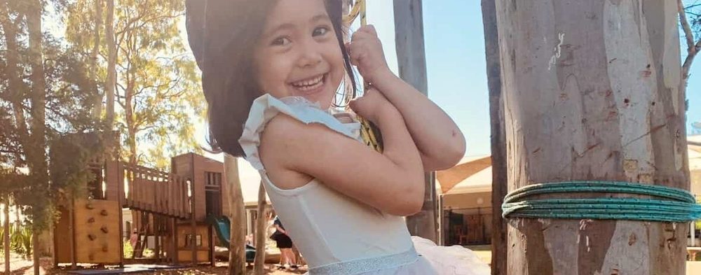 Smiling child holding on to a rope swing between trees